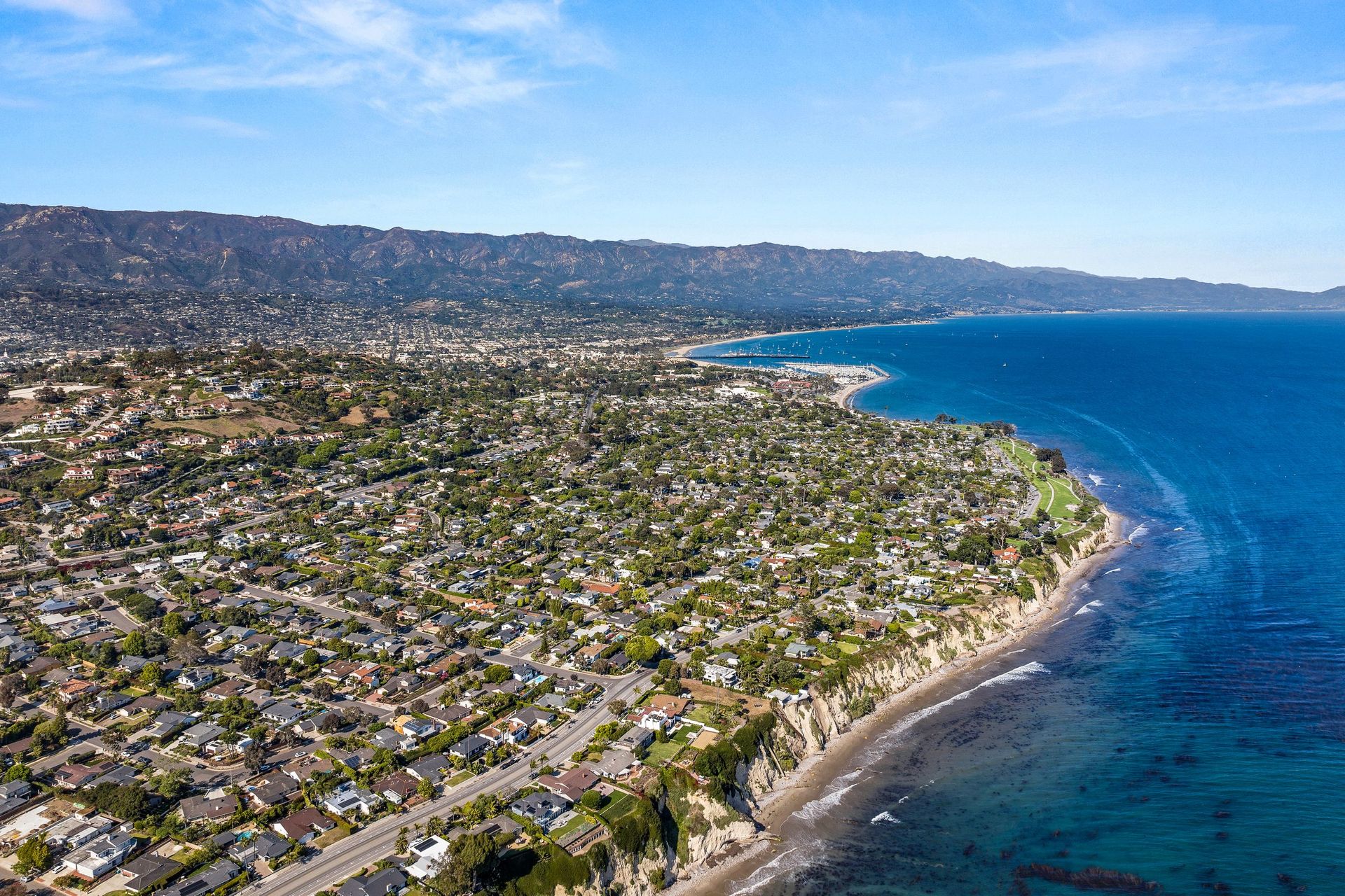 Aerial view along the Santa Barbara coastline toward the harbor, with the Santa Ynez Mountains behind